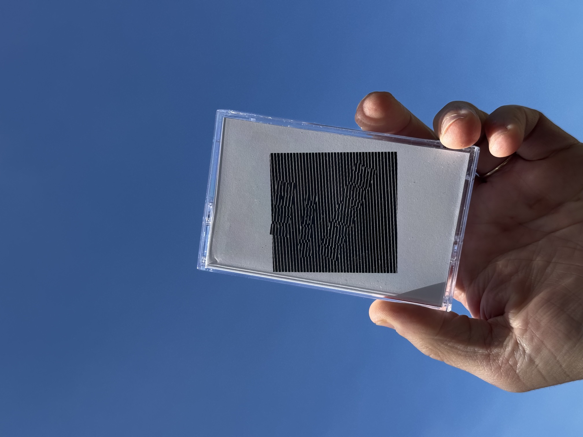 Free Music Ensemble - Social Credit cassette held up against blue sky